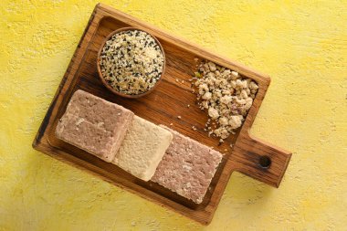 Wooden board with bowl of sesame seeds and sweet halva on color background