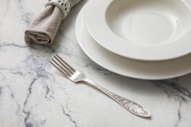 Fork, plates and napkin with gypsophila flowers on white marble table