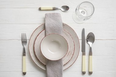 Simple table setting with plates and cutlery on white wooden background