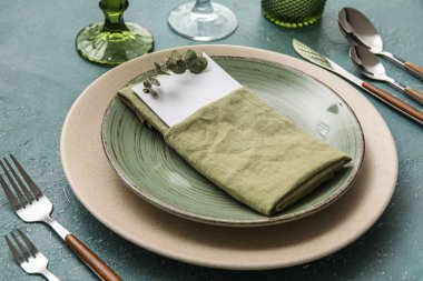 Elegant dinnerware with eucalyptus branch and blank card on color table, closeup