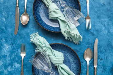 Stylish table setting with plates, napkin and cutlery on blue background