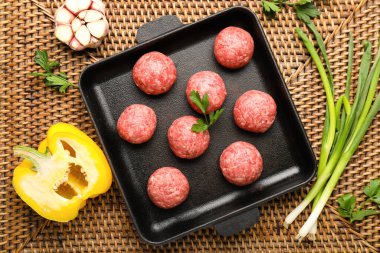 Baking dish with raw meat balls and vegetables on wicker mat