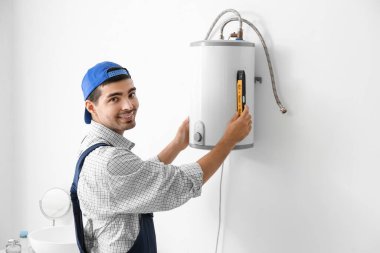 Young plumber installing boiler in bathroom
