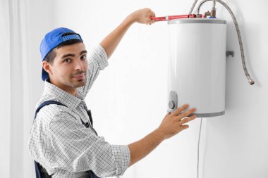 Young plumber repairing boiler with pipe wrench in bathroom