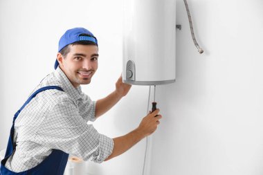 Young plumber repairing boiler with screwdriver in bathroom