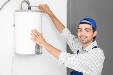 Young plumber repairing boiler with wrench in bathroom