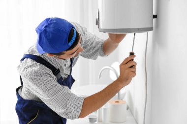 Young plumber repairing boiler with screwdriver in bathroom