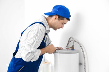 Young plumber repairing boiler with wrench in bathroom