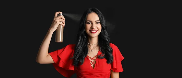 Beautiful young woman with hair spray on dark background