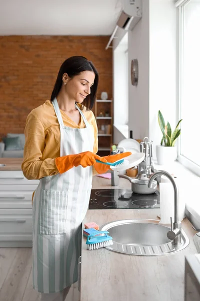 Young woman cleaning plate with brush in kitchen