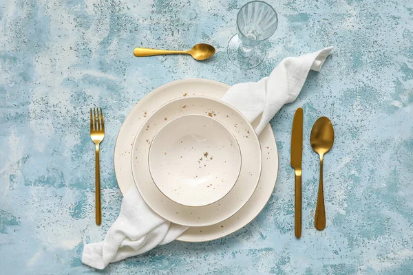 Simple table setting with plates, cutlery and glass on blue background