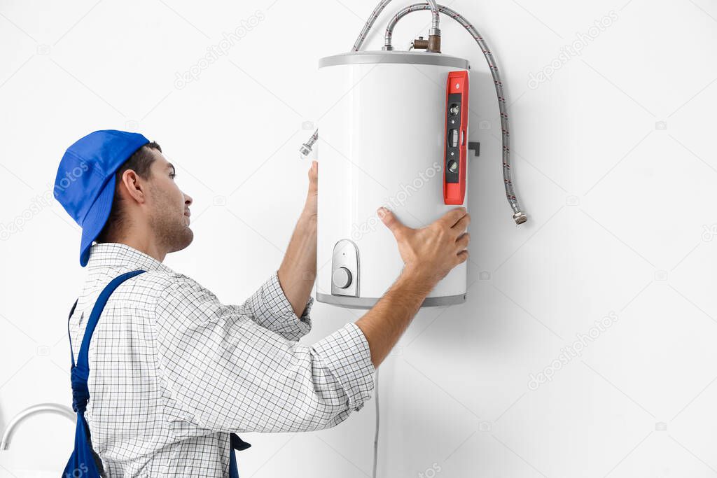 Young plumber installing boiler in bathroom