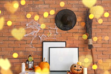 Blank frames with Halloween decor on table near brick wall in room