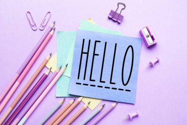 Sticky note with word HELLO and stationery on lilac background