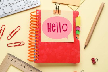 Sticky note with word HELLO, stationery and PC keyboard on yellow background