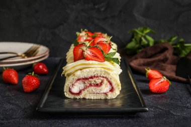 Board with delicious strawberry roll cake on dark background
