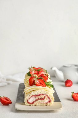 Plate with tasty strawberry roll cake on light background