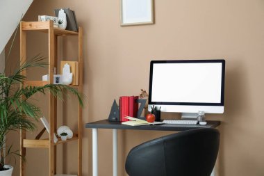 Modern workplace with computer, bookend, apple and pen cup near beige wall in room