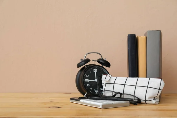 Pencil case with calculator, eyeglasses, books and alarm clock on table against beige background