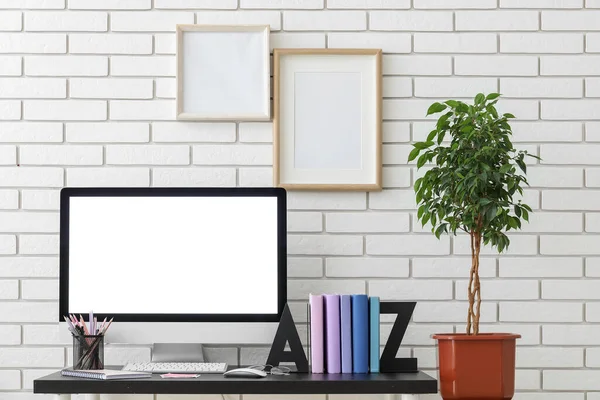 Stylish holder with books, eyeglasses and computer on table near white brick wall