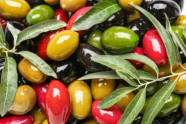 Different kinds of tasty olives and leaves as background, closeup