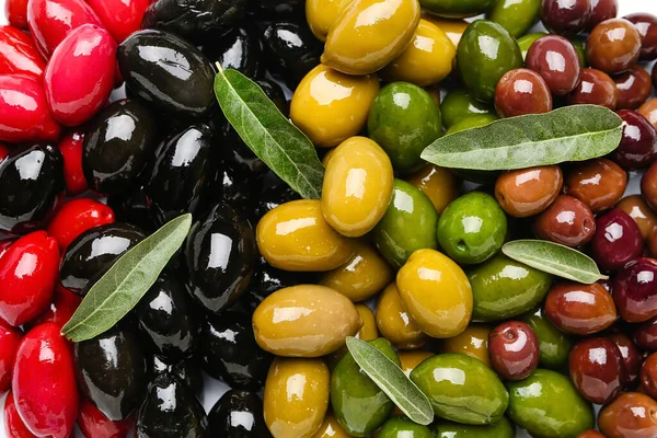 Different kinds of tasty olives and leaves as background, closeup