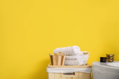 Sarı duvarın yanında havlu ve banyo aksesuarlarıyla dolu bir sepet.