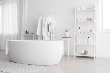 Modern küveti olan şık bir banyo ve beyaz duvarın yanında aksesuarları olan raf üniteleri.