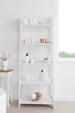 Değişik banyo aksesuarları ve beyaz duvarın yanındaki masada çiçekli vazo.