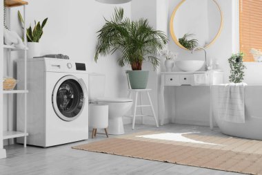 Modern çamaşır makinesi ve küveti olan hafif bir banyo.