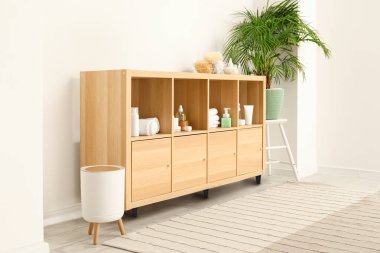 Değişik banyo aksesuarları ve banyo iç tarafındaki beyaz duvarın yanında bitki örtüsü olan raflar.