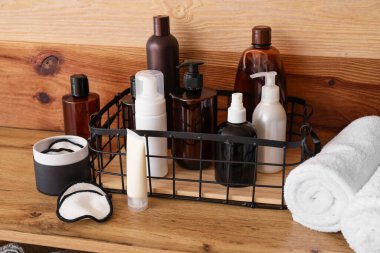 Ahşap duvarın yanındaki rafta farklı banyo aksesuarları var.