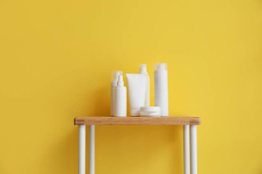 Banyo aksesuarları sarı duvarın yanındaki ahşap rafta.