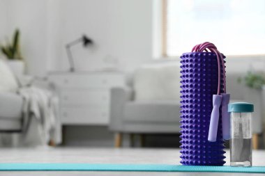 Foam roller with skipping rope and bottle of water on mat in living room