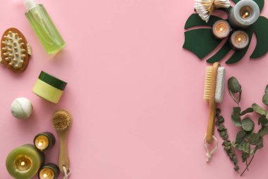 Banyo aksesuarları, kozmetik ürünleri ve pembe arka planda yanan mumlar.