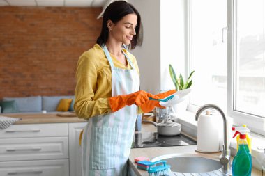 Young woman cleaning plate with brush in kitchen