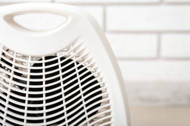 Beyaz tuğla duvarın yanında elektrikli pervane ısıtıcısı, yakın plan.