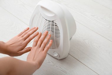 Evdeki elektrikli fan ısıtıcısının yanında ısınan kadın, yakın çekim.