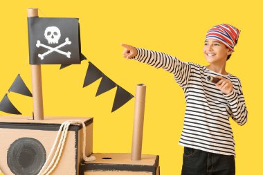 Sarı arka planda dürbünlü ve dürbünlü bir korsan gibi giyinmiş küçük çocuk.