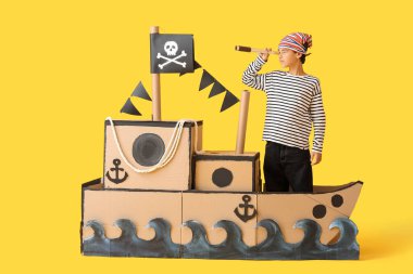 Sarı arka planda dürbünlü ve dürbünlü bir korsan gibi giyinmiş küçük çocuk.