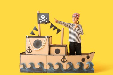 Sarı arka planda dürbünlü ve dürbünlü bir korsan gibi giyinmiş küçük çocuk.