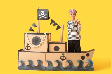 Sarı arka planda dürbünlü ve dürbünlü bir korsan gibi giyinmiş küçük çocuk.