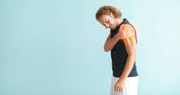 Sporty young man with pain in shoulder on light blue background