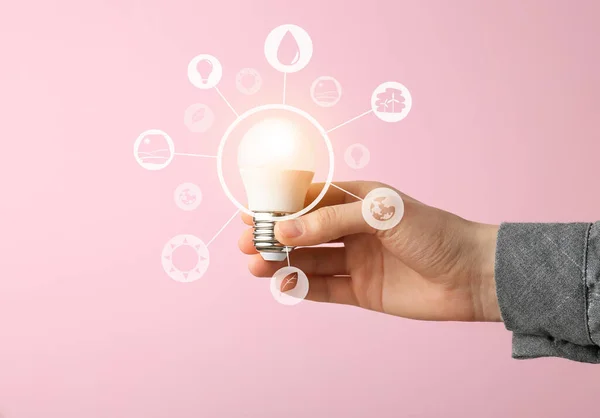 Female hand with light bulb and digital icons on pink background