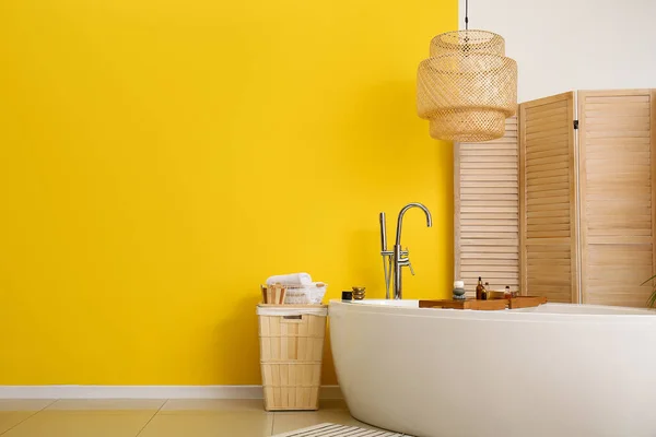 Stylish bathtub, folding screen, lamp and basket near color wall