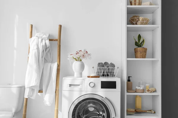 Modern washing machine and shelf unit with bath accessories near white wall