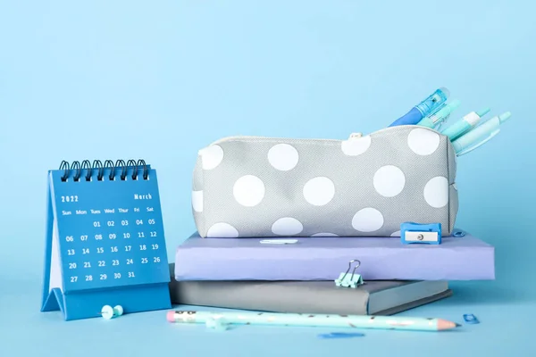 Pencil case with school stationery and calendar on blue background