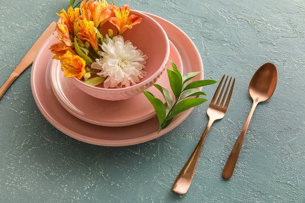 Table setting with beautiful flowers in bowl on green background