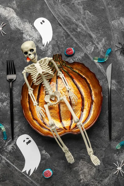 Thematic table setting for Halloween party with skeleton on grunge background