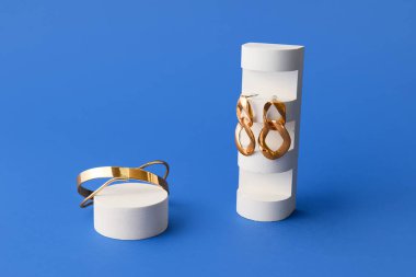 Mavi arka planda zarif küpeleri ve bileziği olan kaideleri göster